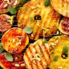 Grilled fruits; pineapples, peaches, figs, pears and watermelon with pine nuts, fresh herbs and honey on the grill plate, top view. Foto: Severin