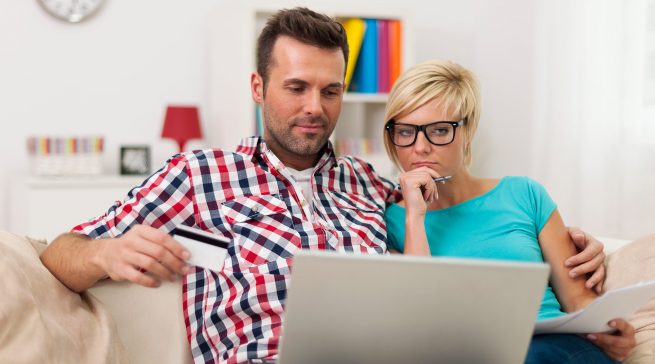 Couple sitting on sofa at home and paying bill on line